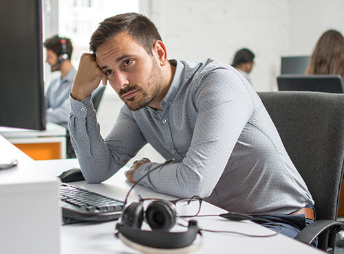Bruit et mauvaise acoustique dans les bureaux et les centres d’appels Un homme assis stressé et fatigué à son poste de travail dans un bureau sans isolation phonique.