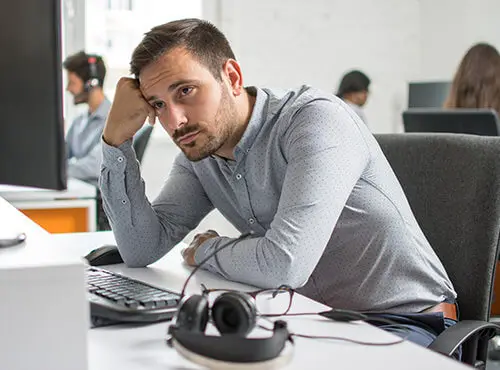 Un homme assis stressé et fatigué à son poste de travail dans un bureau sans isolation phonique.