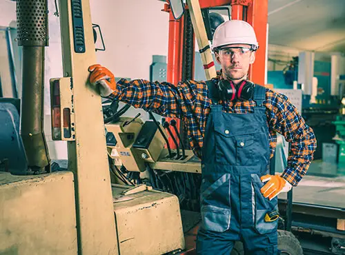 Un travailleur avec des protections auditives se trouve dans un hall industriel ou un atelier bruyant.