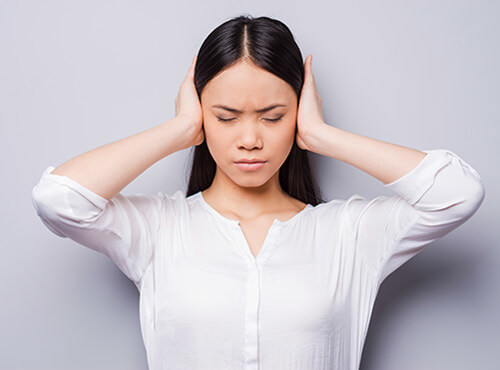Sans isolation phonique le bruit devient une source de stress. Une jeune femme se bouche les oreilles pour ne plus entendre le bruit.